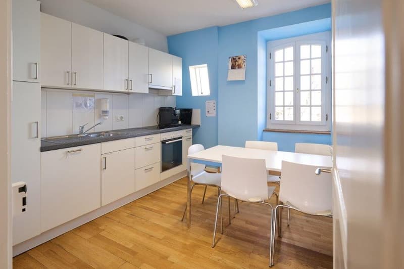 modern kitchen with wooden floors, blue walls, dining area with table and chairs, white cabinets, stove, and sink with faucet