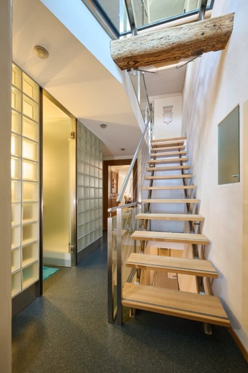 hallway with wooden stairs and metal railing, glass wall with yellow lighting