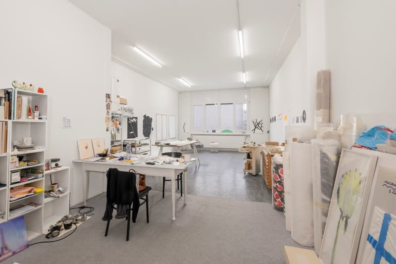 large room, white walls, white ceiling, white desks, white shelves, black chairs, various art supplies, windows