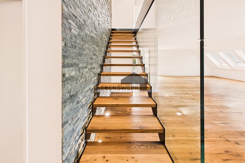 Freitragende Holztreppe mit Glasgeländer und markanter Natursteinwand