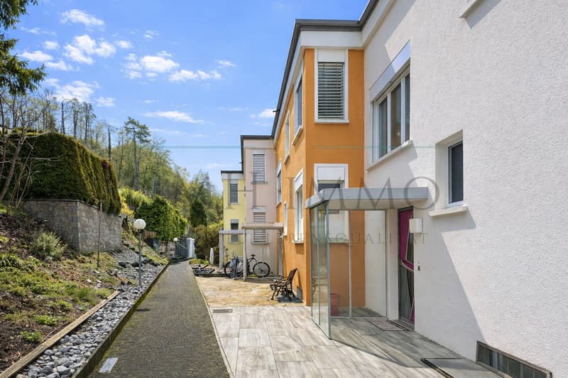 Modern apartment building, white and orange exterior, wooden walkway, bicycles parked, glass entrance, small garden area