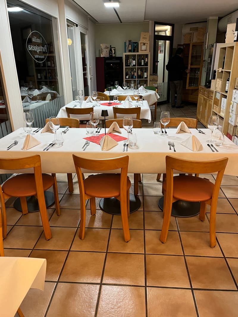 restaurant interior, large dining table set for multiple guests, shelves with wine bottles, white tablecloths, orange chairs, tiled floor