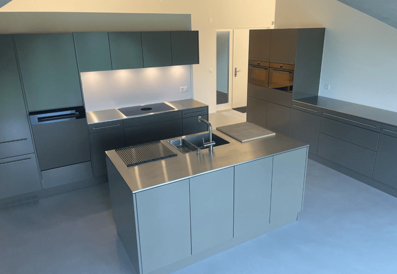 modern kitchen with gray cabinetry, stainless steel countertops, induction cooktop, kitchen island with sink and faucet, appliances in the right side