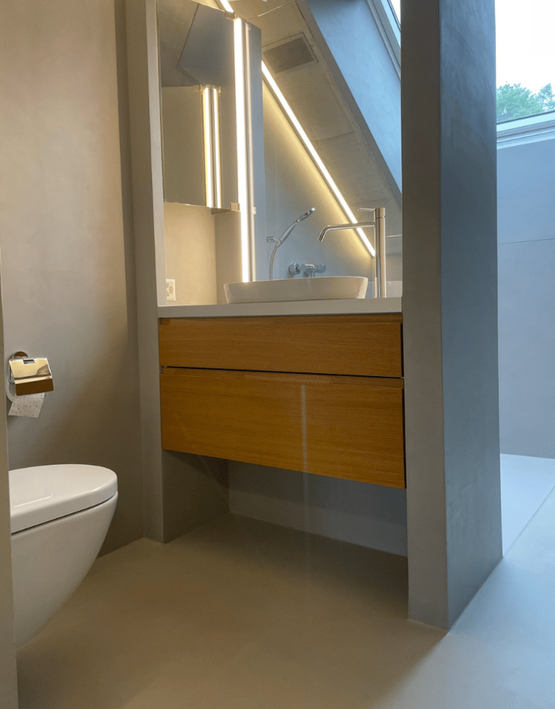Modern bathroom with a toilet, a sink, wooden drawers, and a skylight.