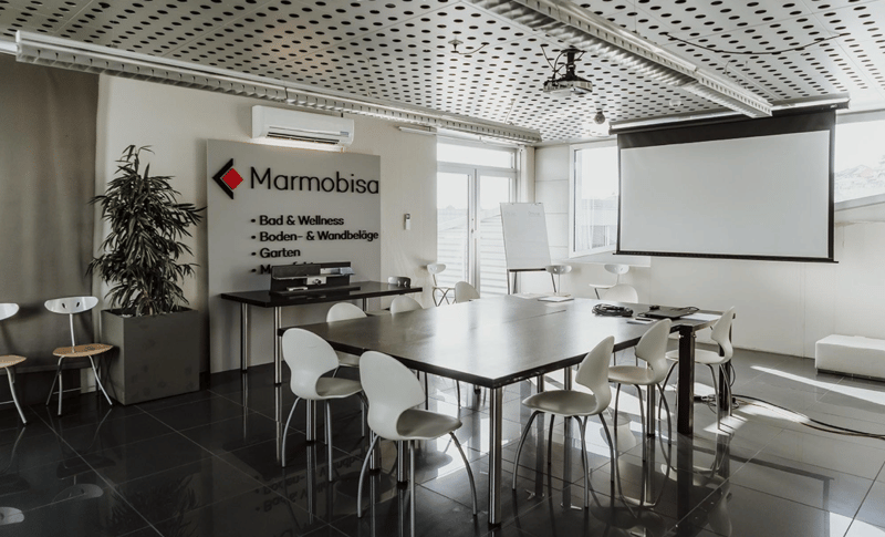 Conference room with desks, chairs, air conditioning, projector screen, whiteboard, and plant