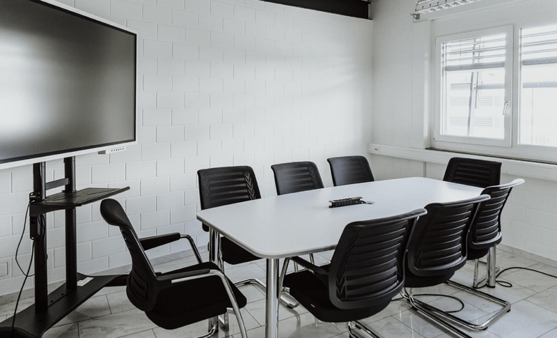 meeting room, white table, black chairs, mounted TV, white walls, windows