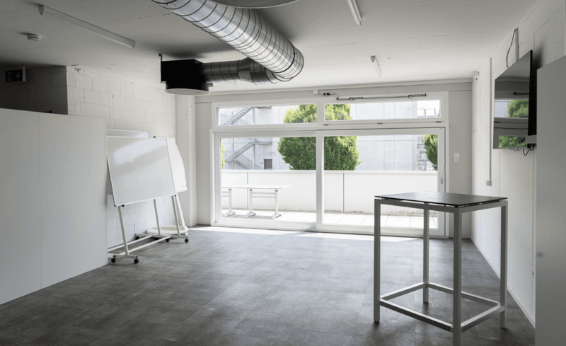 Empty room, concrete floor, sliding glass doors, TV mounted on wall, whiteboard, small table