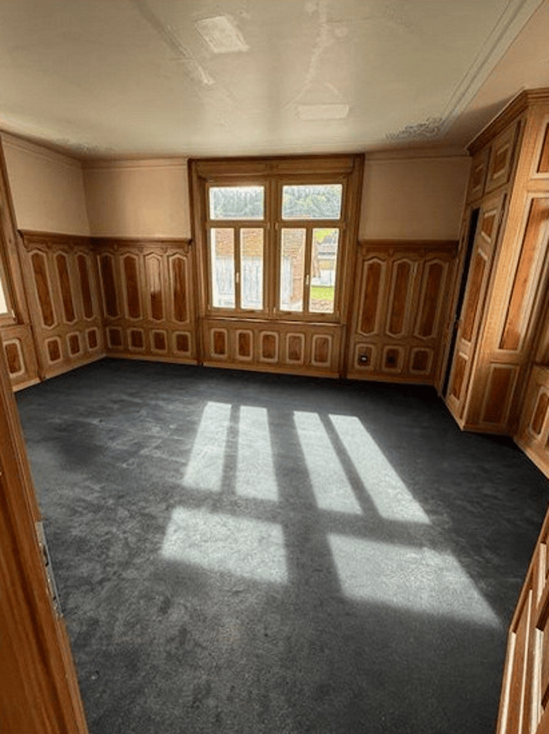 Empty room, wooden walls, carpeted floor, natural light from windows