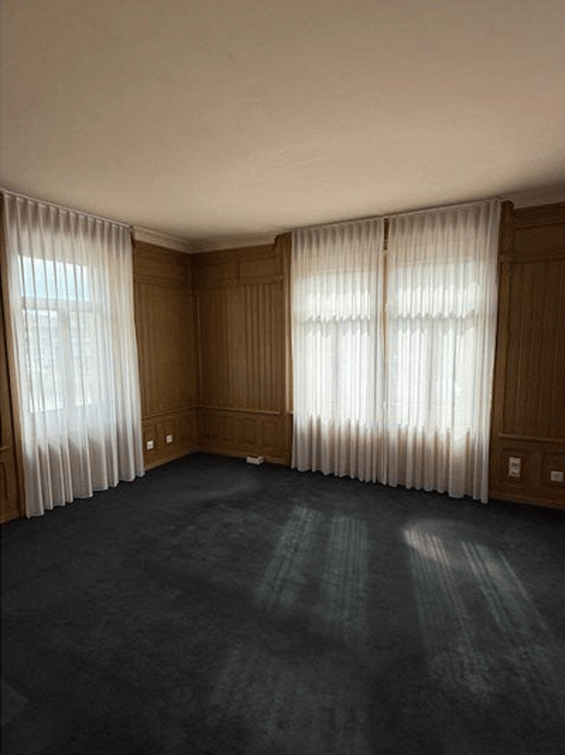 empty room with wooden panels and white curtains on the two large windows