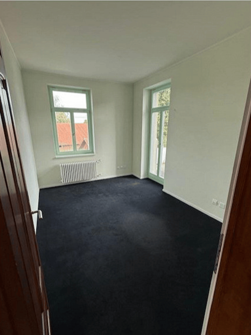 empty room with black carpet, white walls, two glass windows with frames, radiator, floor heating