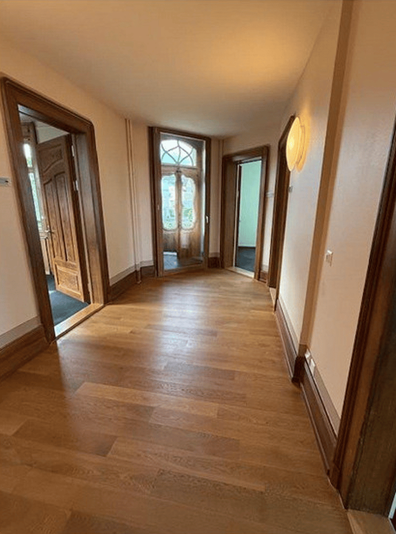 wide hallway, hardwood floors, tall ceilings, light fixtures on the wall
