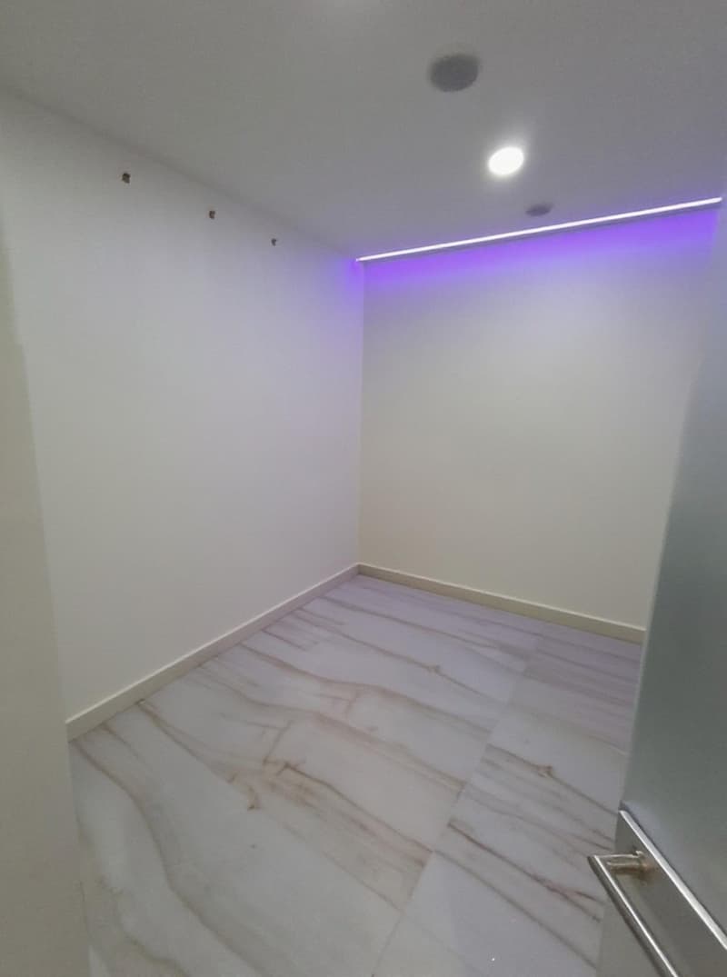 Empty room with white walls and marble flooring, recessed lighting and purple light strip on the ceiling.