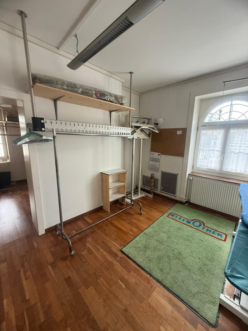 wooden floor, clothes rack, small wooden shelf, green rug, window, radiator