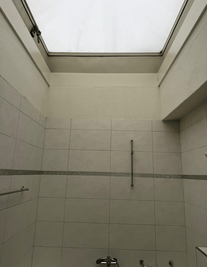 white tiled bathroom, skylight, shower head, towel bar, shower handle, metal drain