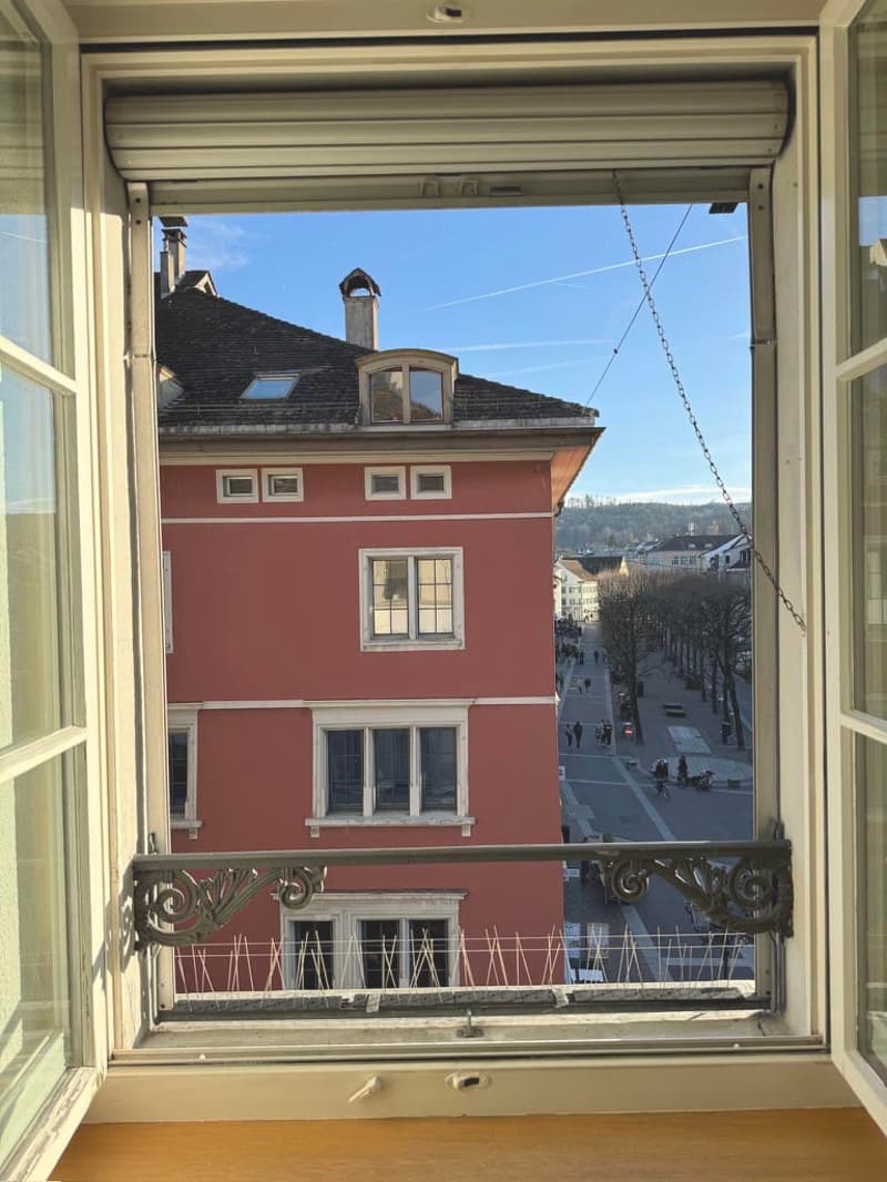 View from window of a red building with multiple windows, people walking on the street