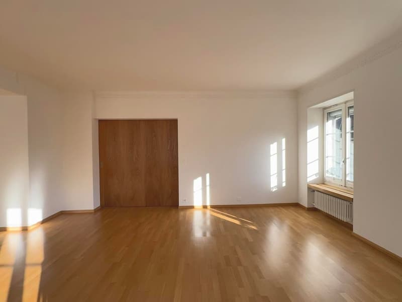 Empty room with hardwood floor, large window, wooden door, and wooden bench under the window