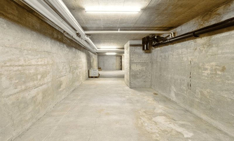 Empty basement with concrete walls and ceiling, white pipes, and fluorescent lighting