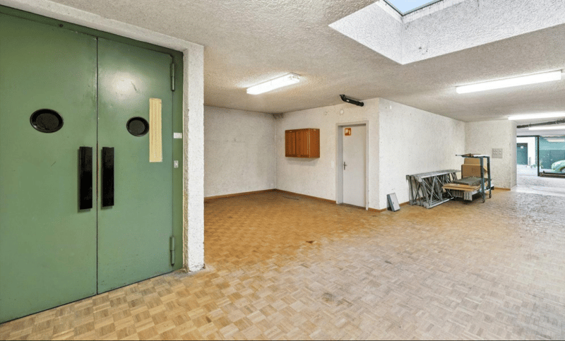 Empty storage room with wooden floor, green doors, mounted light fixtures, a cabinet, and a white door
