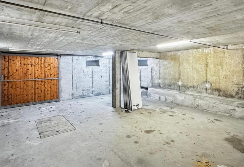 empty garage, wooden gate, exposed ceiling, small white light, open metal doors, concrete walls, floor