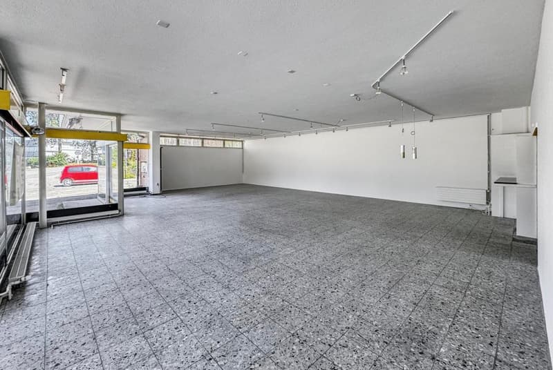 large parking area, tiled floor, large windows, white walls, doors on the left side