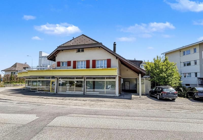 Building with store front, tile roof, yellow awning, street facing, 2 cars parked in front.