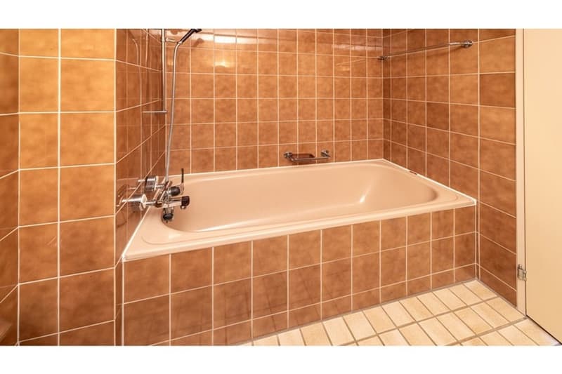 A small, square, bathtub located in the corner of a bathroom with tiled walls.