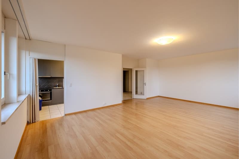 empty room with wooden floor, kitchen, two doors, and an open window to the balcony
