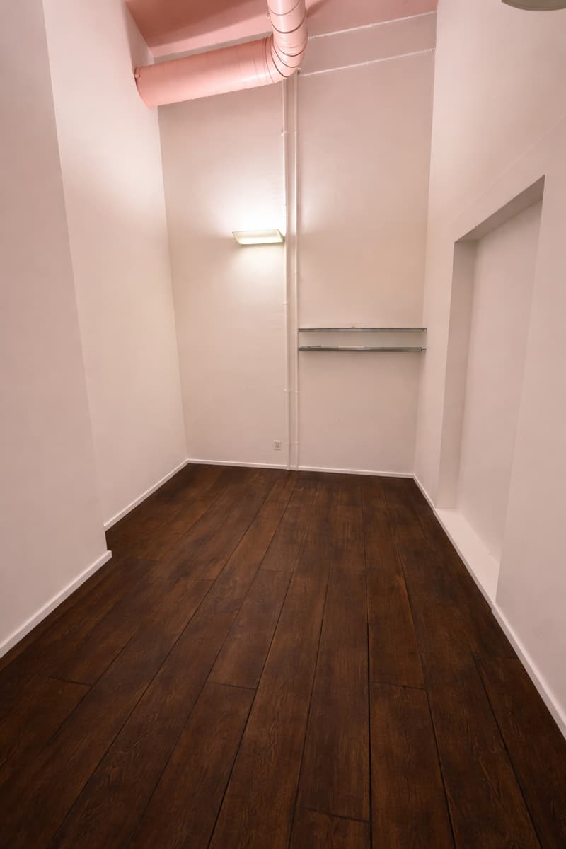 an empty room with wooden flooring, white walls, a single light fixture, and a small glass shelf on the right side