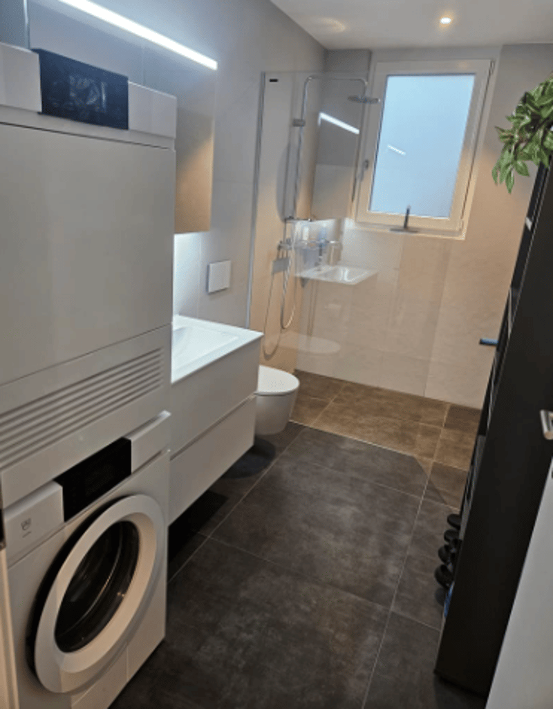 modern bathroom with tile flooring, shower, sink, toilet, and washing machine