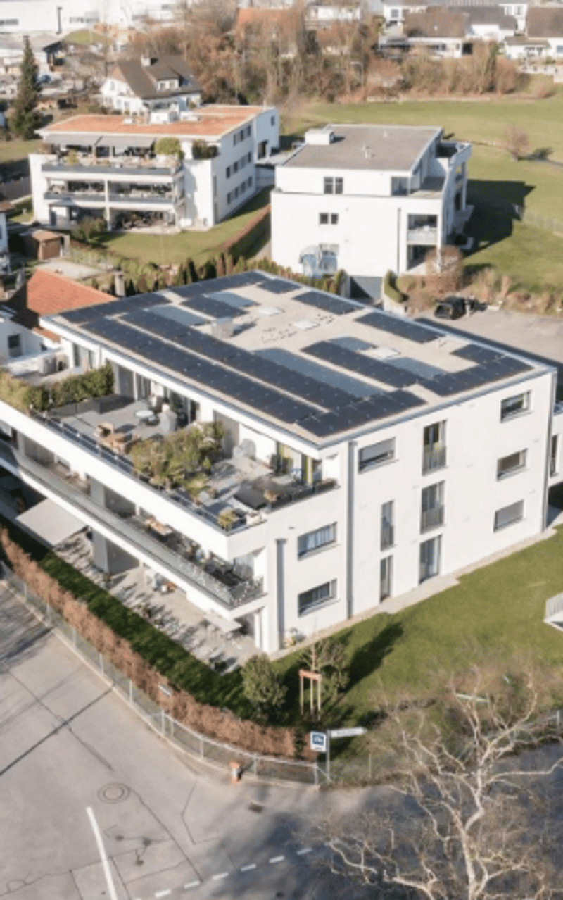 White building, solar panels on the roof, several balconies, ground floor