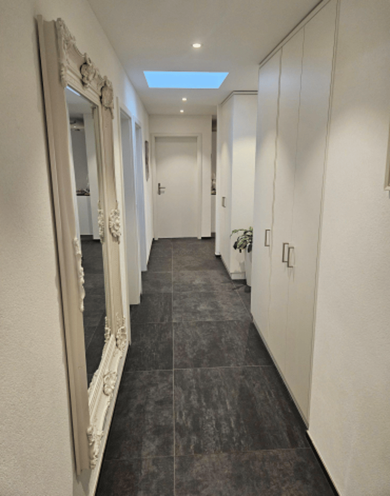 White walls, tiled floor, a large mirror, two rows of wardrobes, a white door