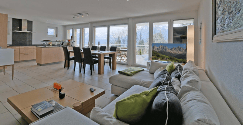 modern living room, grey sofa, dining table with chairs, kitchen, windows