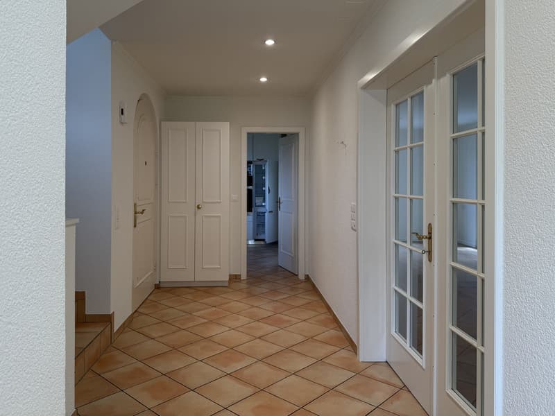 Corridor with white walls, tiled flooring, doors leading to different rooms, bright lighting.