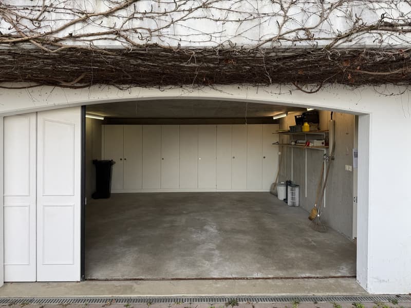 empty garage with storage cabinets, brooms, and a trash can