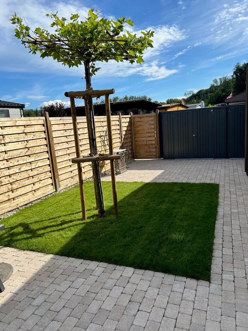 a brick paved garden with a grassy area and wooden fences