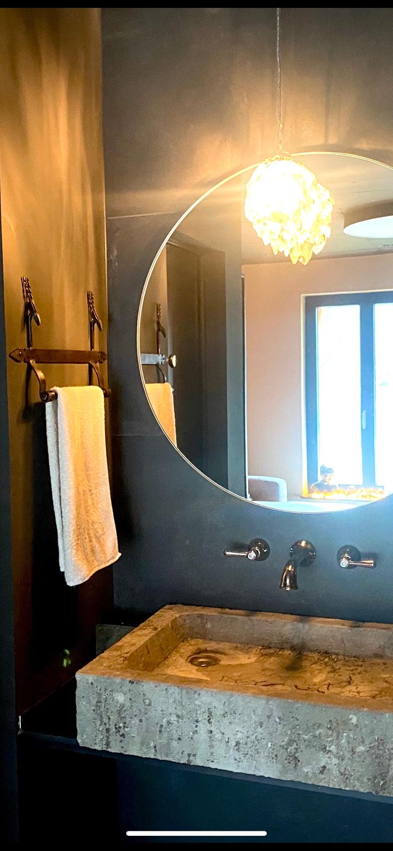 Bathroom with a concrete sink, large mirror, faucet, towel rack, chandelier.