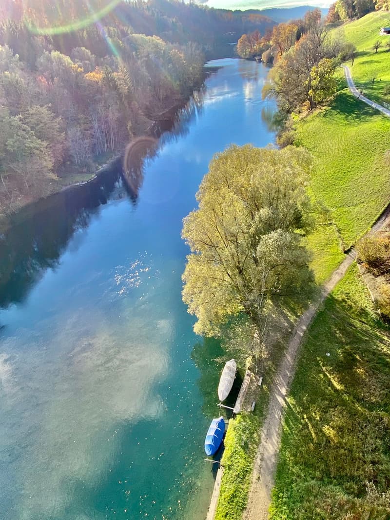Aerial view of a river with a boat and a dock along the riverbank with greenery and a dirt path.