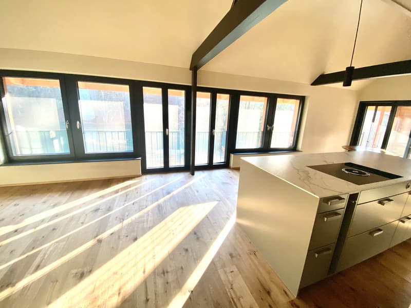 Empty room with kitchen island, hardwood floors, large windows, open doors, sunlight.
