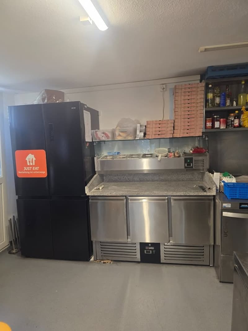 Commercial kitchen with stainless steel appliances, refrigerators, and storage shelves.