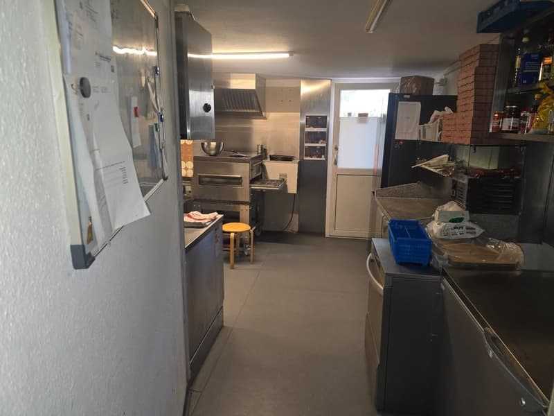 Commercial kitchen with stainless steel appliances, oven, refrigerator, and storage shelves.