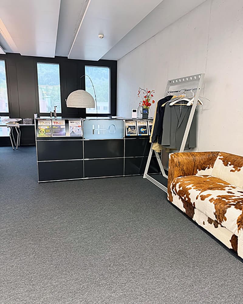 a reception area, with a reception desk, books, magazines, a lamp, a coat rack, and a sofa