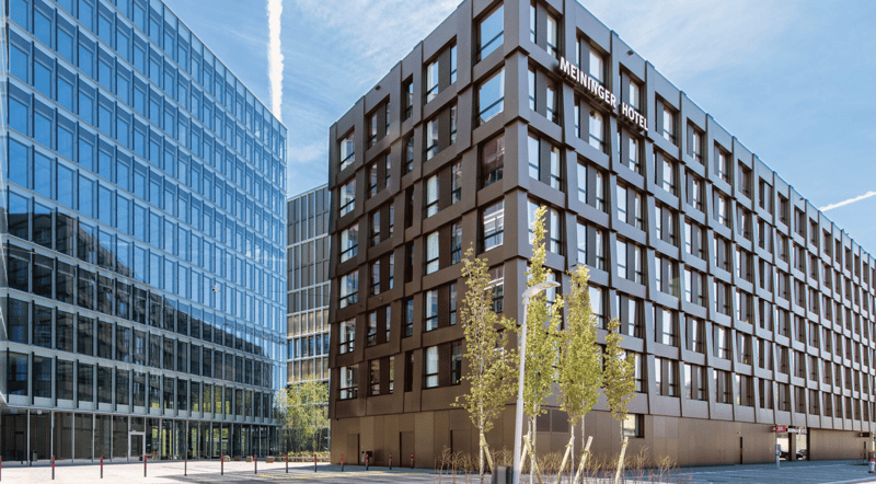 Modern building with glass facade, brown facade, multiple windows, trees, street lights, parking area