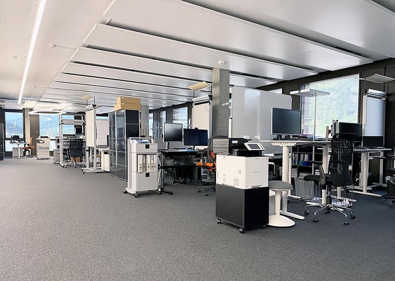An empty office space with multiple tables, chairs, and monitors.