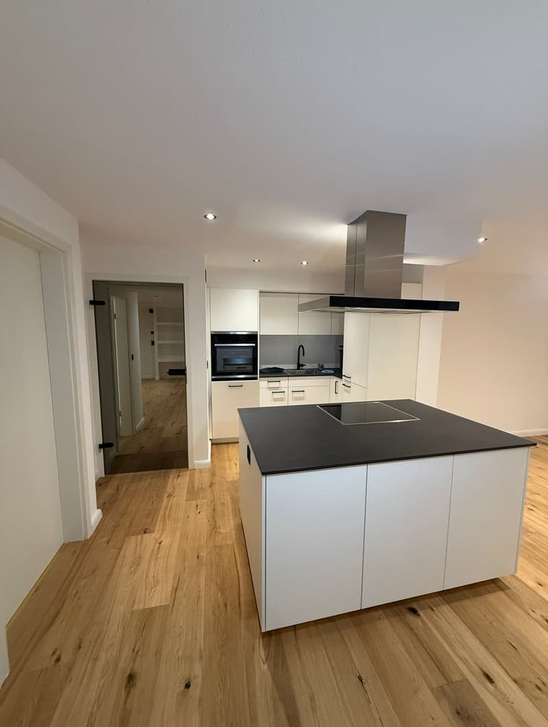 modern kitchen with white cabinets, black countertop, island with induction cooktop, built-in oven, extractor hood, wooden floor