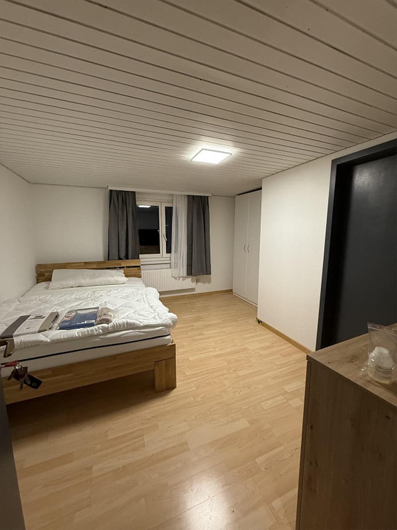 Bed, white bedsheet, pillows, wooden floor, window with curtains, built-in wardrobe, wooden desk