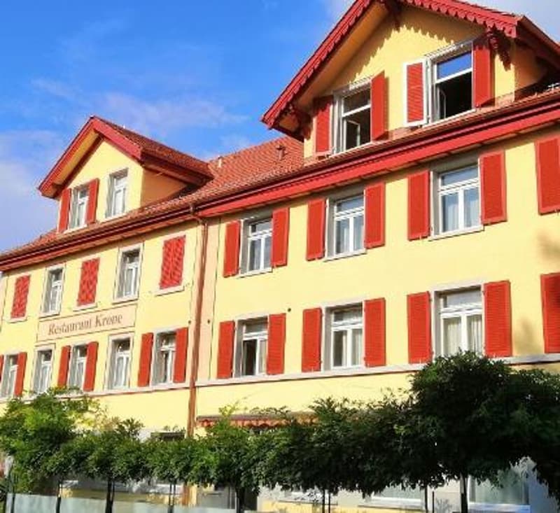 3 story yellow building, red trim, multiple windows, red shutters, tree in front