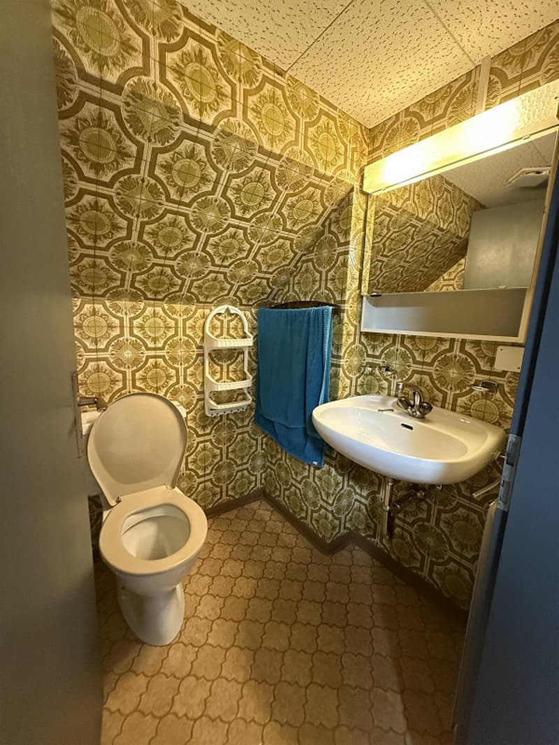 a toilet, sink, and mirror with decorative tiled walls, with an open door