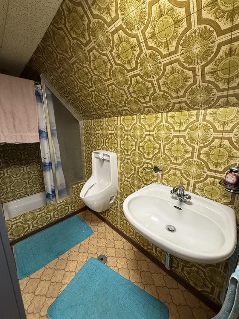 Decorated with green wall tiles and blue rug, bathtub, sink, and urinal.