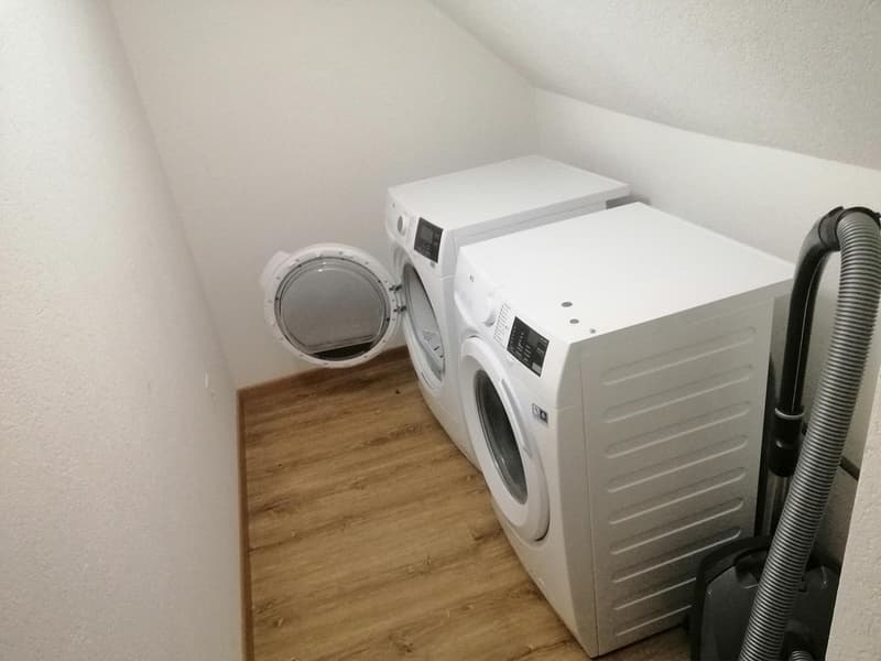 2 washing machines, wooden floor, white walls, black vacuum cleaner