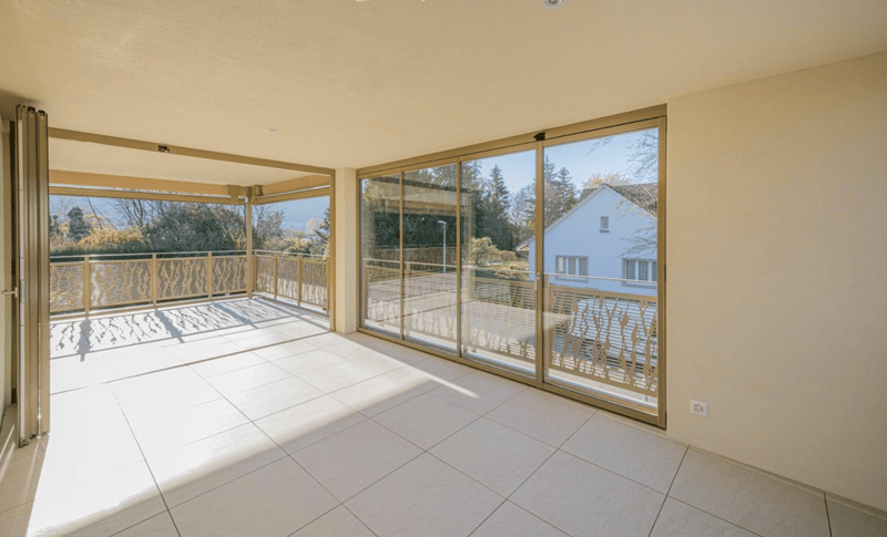 large balcony, sliding glass doors, tiled floor, metal railings, view of trees and house